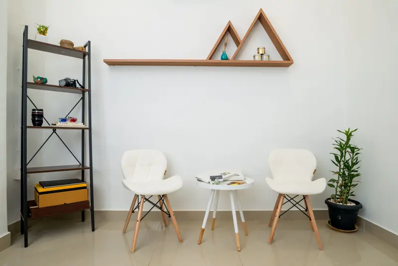 Two white chairs and a small round table under a wooden mountain-shaped shelf